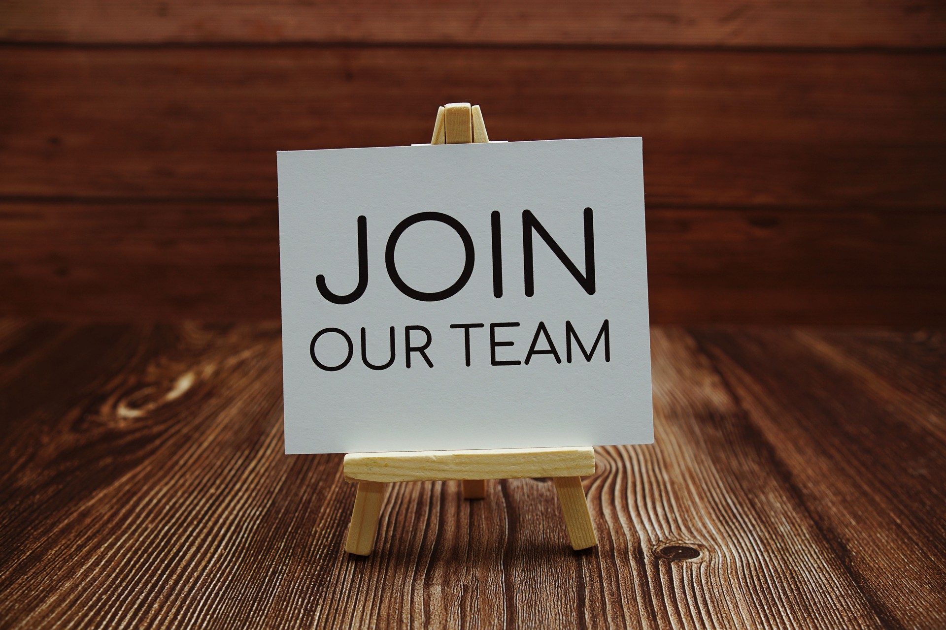 Join Our Team text on paper card on wooden background Join Our Team text on paper card on wooden background